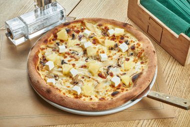 Beyaz soslu iştah açıcı pizza, tavuk, ananas ve ahşap zemin üzerinde çıtır çıtır mantar. Restoran masası. Kapat.