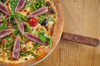 Ton balığı, roka, vişneli domates ve ahşap zemin üzerinde çıtır çıtır parmesanlı iştah açıcı pizza. Restoran servisi. Deniz mahsullü pizza. Üst görünüm