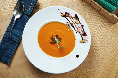 Taze, sebzeli balkabağı kremalı çorba, beyaz tabakta, ahşap zemin üzerinde. Restoran masası ayarı