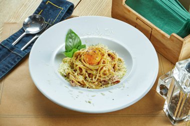 Beyaz bir tabakta yumurta sarısı, pastırma ve parmesan peynirli ev yapımı İtalyan carbonara makarnası (spagetti). Restoran masası ayarı
