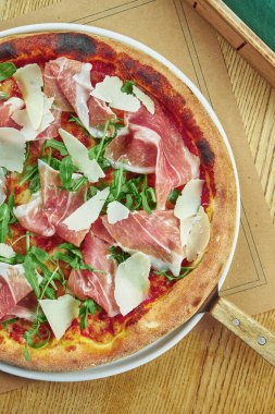 Prosciutto di parma, parmesan peyniri ve ahşap zemin üzerinde çıtır çıtır roka ile aperatif pizza. Restoran masası. Üst görünüm