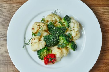 Diyet ve vejetaryen atıştırmalıkları (brokoli, karnabahar ve kiraz domatesleri) beyaz bir tabakta ahşap bir arka planda.