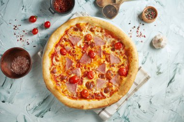 Çeri domatesli çıtır çıtır pizza, mozzarella ve jambon gri bir zemin üzerinde malzeme ve mutfak gereçleri ile kompozisyonda.