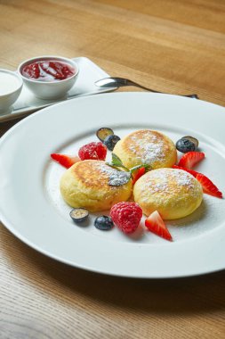 Klasik Ukrayna şurubu, böğürtlen, reçel ve ekşi krema ile ahşap bir arka planda beyaz bir tabakta. Kahvaltılık iştah açıcı tatlı.