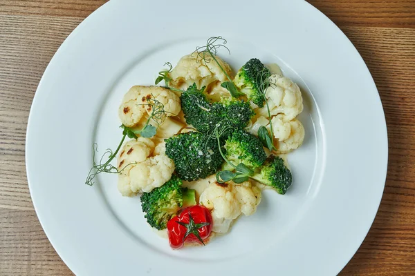 Diet and veggie snack - steamed vegetables (broccoli, cauliflower and cherry tomatoes) in a white plate on a wooden background