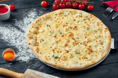 4 çeşit peynirli fırınlanmış pizza, beyaz sos ve malzemelerle birlikte siyah ahşap arka planda. Üst görünüm