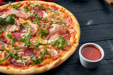 Salamlı fırınlanmış pizza, prosciutto ve kırmızı soslu tavuk ve siyah ahşap bir arka planda eritilmiş peynir içerikli kompozisyon. Üst görünüm