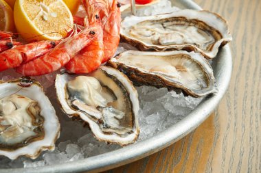 Buzlu bir tabakta taze pişmiş deniz ürünleri. Taze istiridye ve karides. Yakın görünüm, seçici odak, tahta arkaplan