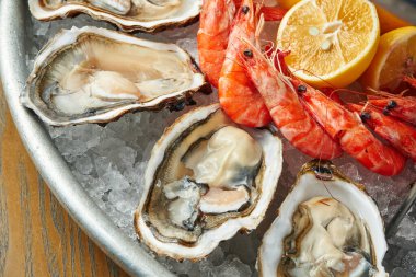 Buzlu bir tabakta taze pişmiş deniz ürünleri. Taze istiridye ve karides. Yakın görünüm, seçici odak, tahta arkaplan
