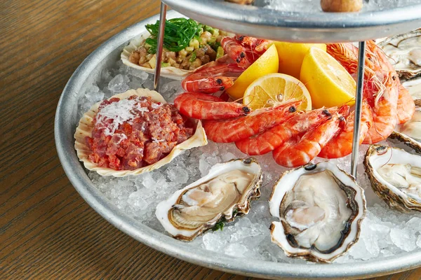 Close up view on tasty plate with seafood on ice - tuna tartar in a shell, shrimp, oysters. Healthy Antipasti. Wooden background. Selective focus