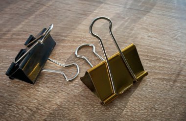 İki ataç altın ve siyah, ofis kırtasiyesi için Bulldog şarjörü, masanın arkasında.