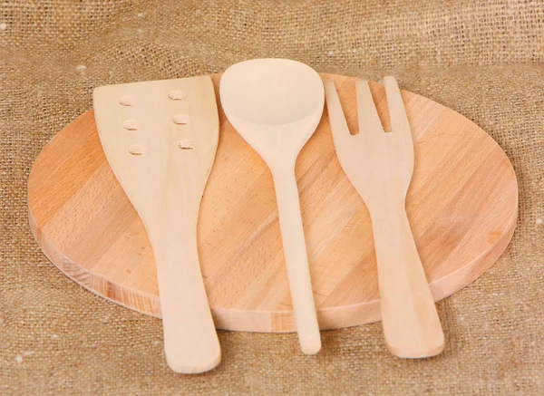 A spoon, a fork and a spatula made of wood. The concept of cooking. A curled instrument lies on a background of rough fabric. Horizontal image.