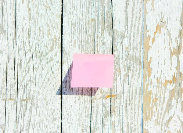 Pink sticker on old wooden background. Texture of white painted boards. Sheet of paper on the fence. Horizontal image. Free space for text.