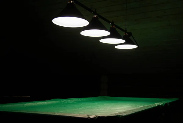 Pool table lit by lamps on a dark background. Low key shooting in low light