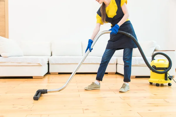 Professioneller Reinigungsservice. Frau in Uniform und Handschuhen putzt in einer Hütte. der Arbeiter saugt den Boden mit professionellem Gerät — Stockfoto