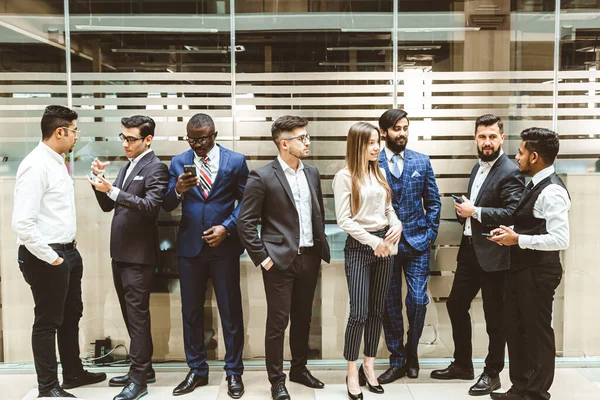 Jóvenes empresarios están de pie y hablando en el fondo de las oficinas de vidrio. Corporativossteam y gerente en una reunión. — Foto de Stock