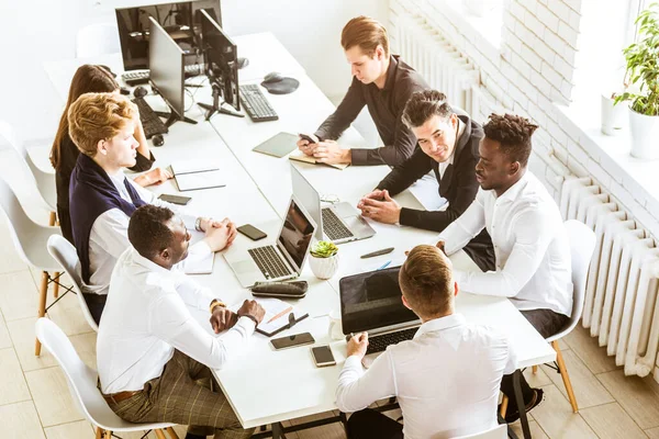 Un equipo de jóvenes empresarios sentados a la mesa, con vista superior, trabajando y comunicándose juntos en una oficina. Corporativossteam y gerente en una reunión . — Foto de Stock