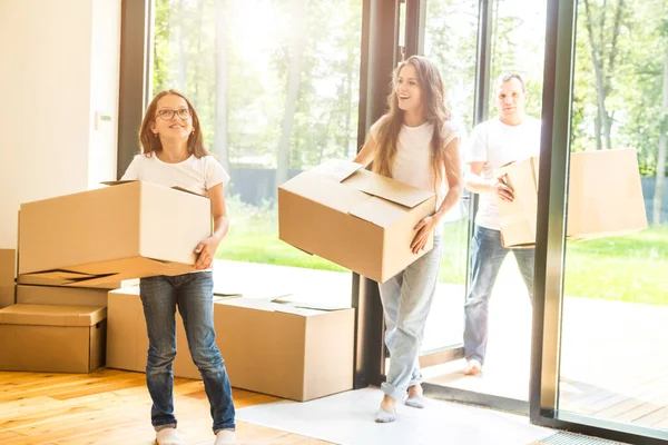 Giovane famiglia felice, i genitori figlia e figlio, disfare le scatole e trasferirsi in una nuova casa. bambini divertenti corrono dentro con scatole — Foto Stock