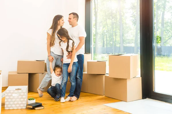 Feliz familia joven, padres hija e hijo, desempacando cajas y mudarse a un nuevo hogar. niños divertidos corren con cajas — Foto de Stock