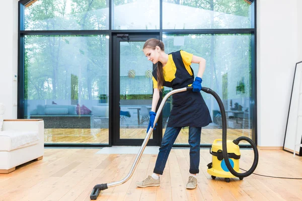 professional cleaning service. woman in uniform and gloves does the cleaning in a cottage. the worker vacuums the floor with professional equipment