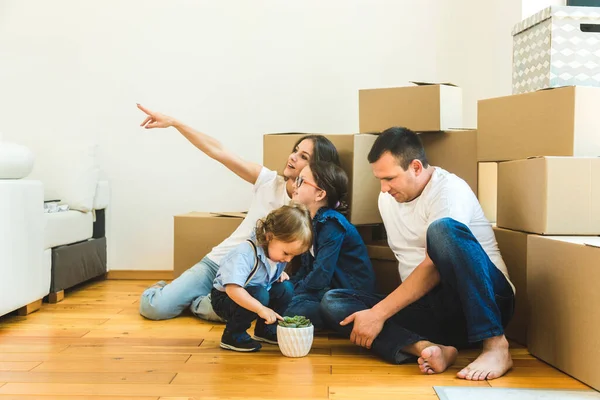 Feliz familia joven, padres hija e hijo, desempacando cajas y mudarse a un nuevo hogar. niños divertidos corren con cajas — Foto de Stock