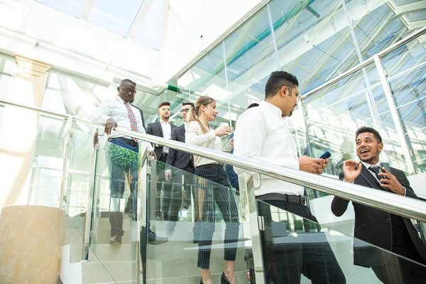 Jóvenes empresarios arego abajo de las escaleras y hablando en el fondo de las oficinas de vidrio. Corporativossteam y gerente en una reunión. — Foto de Stock
