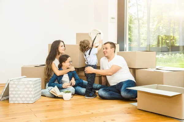 Happy young family, parents daughter and son, unpacking boxes and moving into a new home. funny kids run in with boxes — Stok Foto