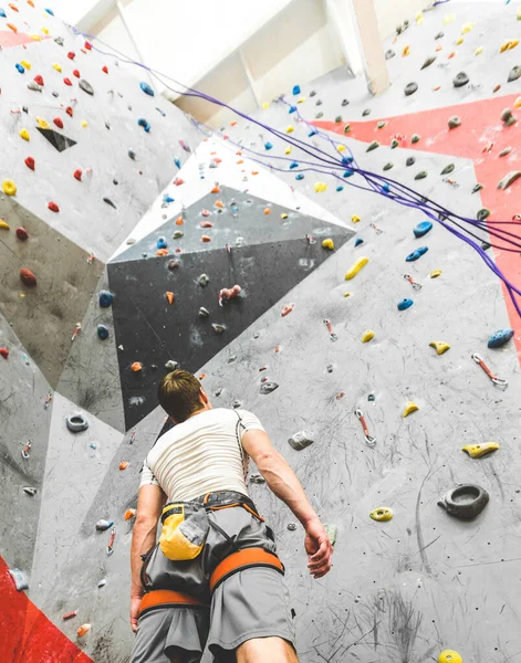Sporcu tırmanışçı dik kayalara bakıyor, içerideki yapay duvara tırmanıyor. Ekstrem spor ve kaya konsepti — Stok fotoğraf