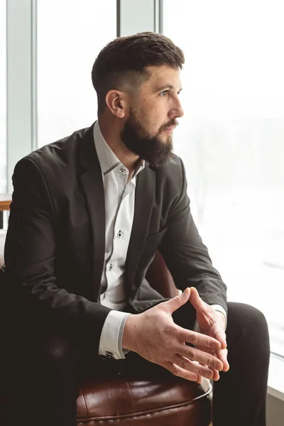 Retrato de un joven empresario con un traje en la oficina. Primer plano sentado en una silla junto a la ventana — Foto de Stock