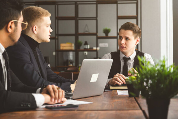 A team of young businessmen in suits working and communicating together in an office. Corporate businessteam and manager in a meeting.