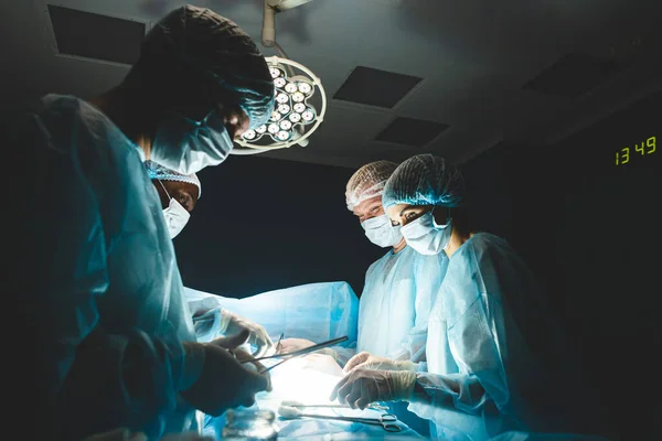 Une équipe internationale de chirurgiens, d'assistants et d'anesthésistes effectue une opération complexe sur un patient sous anesthésie générale. Thème de la photographie atmosphérique sombre en mode discret. — Photo