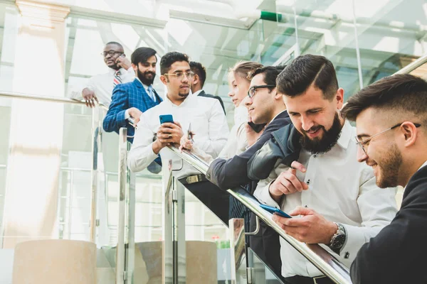 Jóvenes empresarios arego abajo de las escaleras y hablando en el fondo de las oficinas de vidrio. Corporativossteam y gerente en una reunión. — Foto de Stock