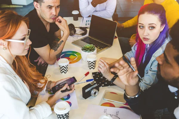 Grupo de ejecutivos multiétnicos discutiendo durante una reunión. Hombre y mujer de negocios sentados alrededor de la mesa en la oficina y sonriendo. Un equipo de jóvenes diseñadores creativos — Foto de Stock