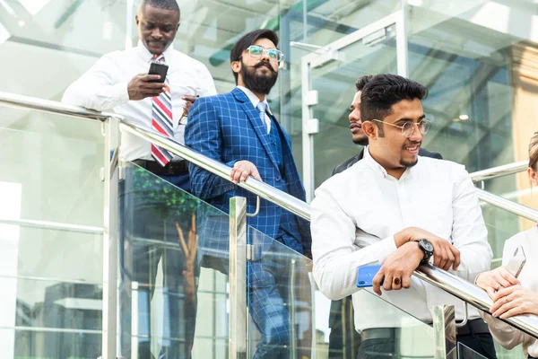 Jóvenes empresarios arego abajo de las escaleras y hablando en el fondo de las oficinas de vidrio. Corporativossteam y gerente en una reunión. — Foto de Stock