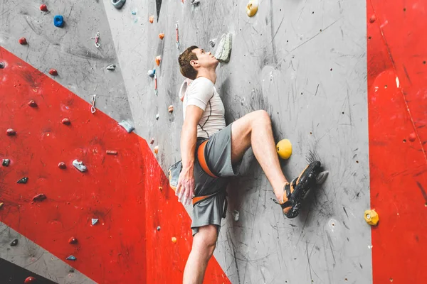 Спортсмен скелелазіння рухається вгору по крутій скелі, сходження на штучну стіну в приміщенні. Концепція екстремальних видів спорту та боулдингу — стокове фото