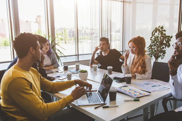 Grupo de ejecutivos multiétnicos discutiendo durante una reunión. Hombre y mujer de negocios sentados alrededor de la mesa en la oficina y sonriendo. Un equipo de jóvenes diseñadores creativos — Foto de Stock