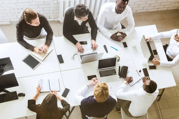 Un equipo de jóvenes empresarios sentados a la mesa, con vista superior, trabajando y comunicándose juntos en una oficina. Corporativossteam y gerente en una reunión . — Foto de Stock