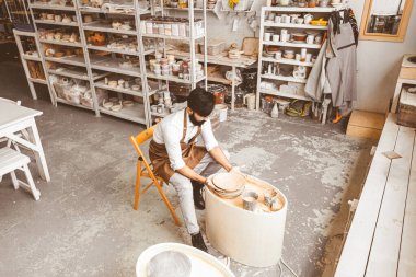 Genç bir erkek çömlekçi atölyesinde çömlekçi çarkında el işi yapıyor ve kilden bir ürün yapıyor.