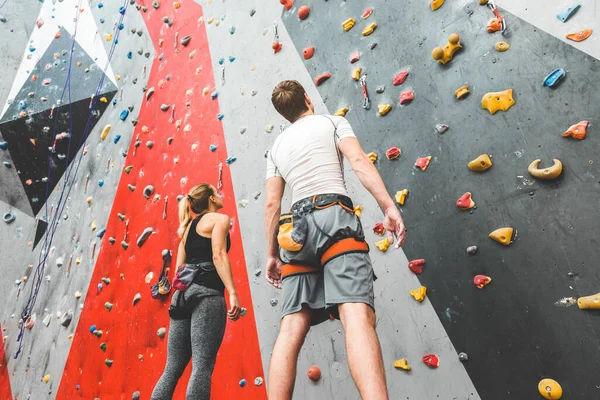 Couple of athletes climber stand and watch on steep rock, climbing on artificial wall indoors. Extreme sports and bouldering concept. — Stock Photo, Image