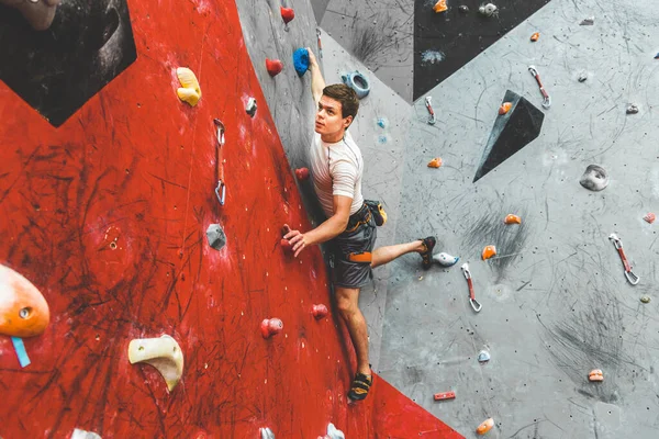 Deportista escalador ascendiendo en roca escarpada, escalando en la pared artificial en el interior. Concepto de deportes extremos y bouldering — Foto de Stock