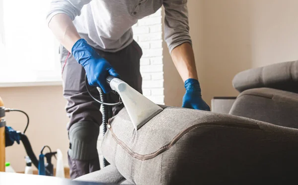 Stomerij man werknemer het verwijderen van vuil uit meubels in flat, close-up, stofzuigen sofa met professionele apparatuur — Stockfoto