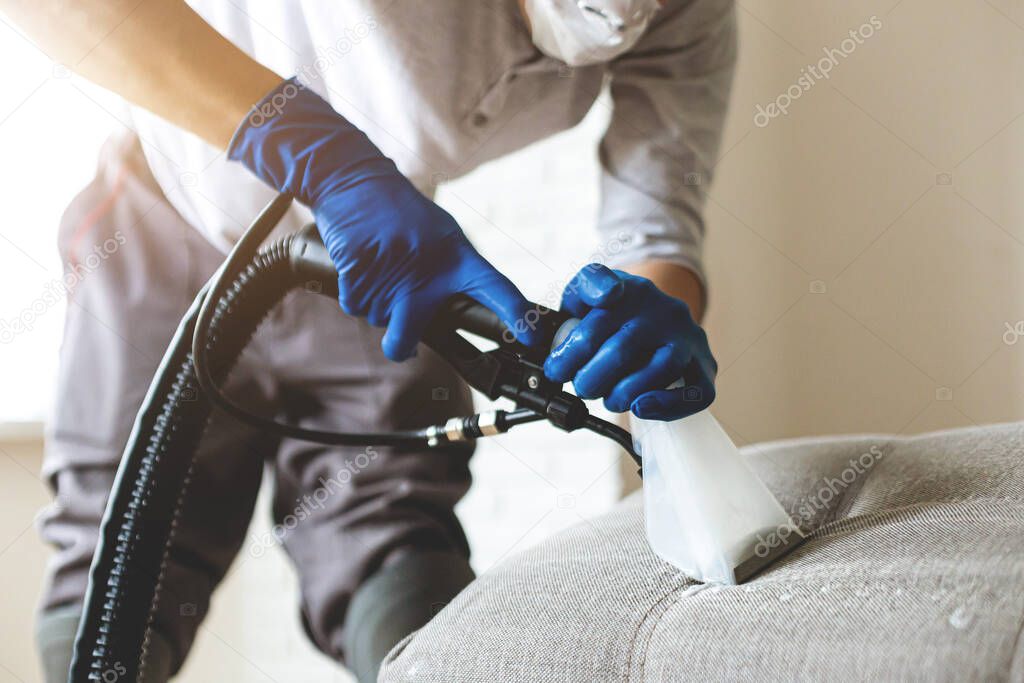 Man dry cleaners employee hand in protective rubber glove cleaning sofa with professionally extraction method. Early spring regular cleanup. Commercial cleaning company concept. Closeup