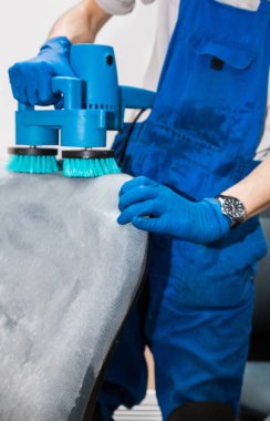 İş elbiseli ve lastik eldivenli genç adam ofis sandalyesini profesyonel ekipmanlarla temizliyor..