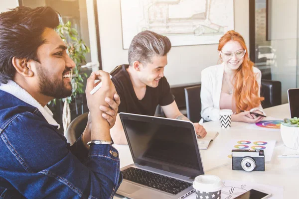 Grupo de ejecutivos multiétnicos discutiendo durante una reunión. Hombre y mujer de negocios sentados alrededor de la mesa en la oficina y sonriendo. Un equipo de jóvenes diseñadores creativos — Foto de Stock