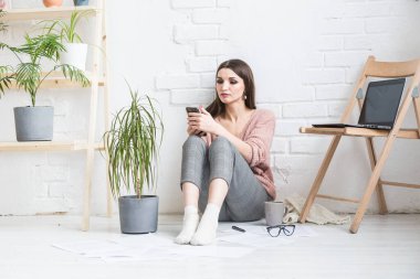 Ev yapımı günlük giysiler içinde mutlu bir kadın parlak bir iç mekanda oturur ve telefon kullanır, kız bir dizüstü bilgisayarda çalışırken ve internette sörf yaparken dinlenir. Rahat serbest çalışma alanı,