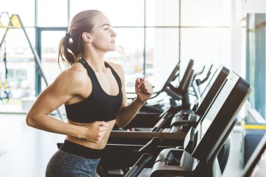Modern spor salonundaki koşu bandında koşan siyah spor giysili atletik kadın.