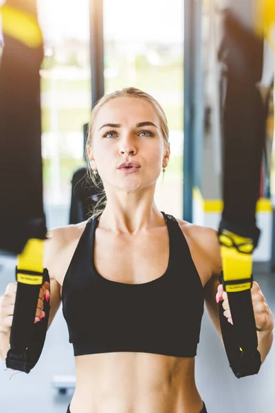 Allenamento femminile con cinghie fitness in palestra. Bella signora che esercita i muscoli fionda o cinghie di sospensione. — Foto Stock