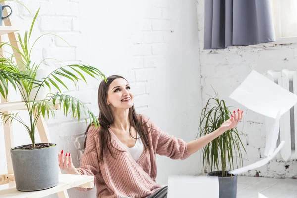 Una joven mujer feliz vomita un montón de papeles y documentos sentados cerca del portátil, la chica independiente está feliz y de buen humor. emoción e inspiración — Foto de Stock