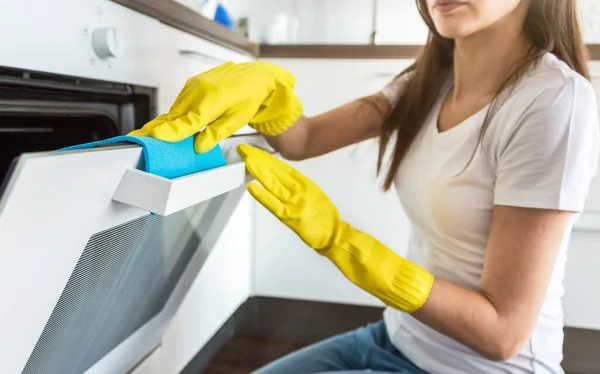 Profesyonel temizlik şirketinden genç bir kadın evi temizliyor. Bir adam mutfağı temizlik malzemeleriyle sarı eldivenlerle yıkıyor.. — Stok fotoğraf