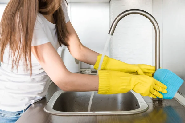 A young woman in yellow gloves washes crane with a sponge in the sink. House professional cleaning service — Stock Photo, Image